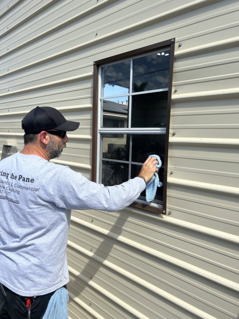 A handyman from Bring The Pane meticulously cleaning an exterior window with a cloth in Lewiston, ID.