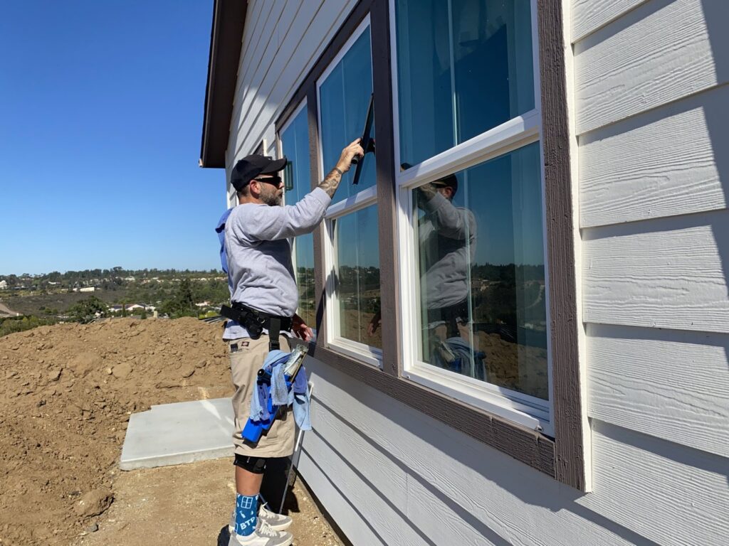 A handyman from Bring The Pane cleaning an exterior window with a squeegee on a new build home in Lewiston, ID.