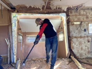 A man using a crowbar to demolish the interior of an old trailer, part of a cleanout service by Hometown Hauling 802 in Milton, VT.