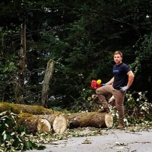 A man standing with a chainsaw next to felled logs and branches, representing tree work by Everybody's Tree Service in Juneau, AK.
