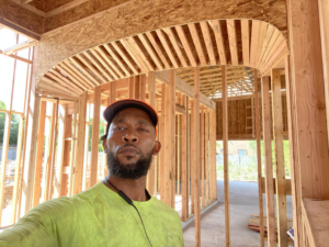A man standing inside a house under construction, showing wooden framing and an arched ceiling, by Antoine Grisby Construction in Gilbert, AZ.