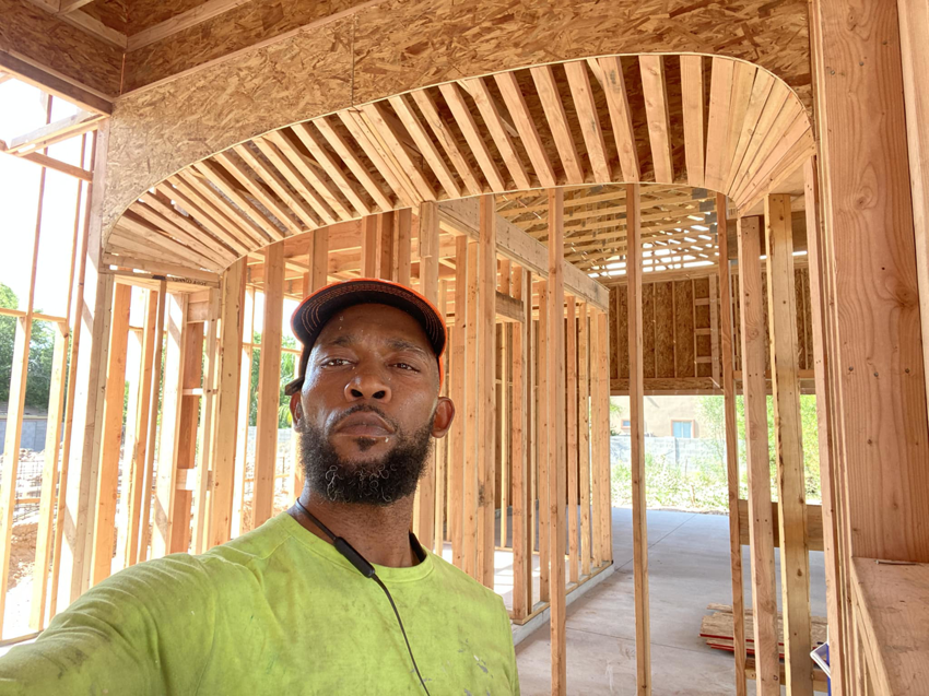 A man standing inside a house under construction, showing wooden framing and an arched ceiling, by Antoine Grisby Construction in Gilbert, AZ.