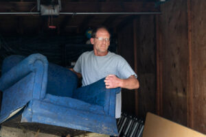 A man moving a blue armchair out of a garage for A1 Junk Removal Of Tucson, AZ.