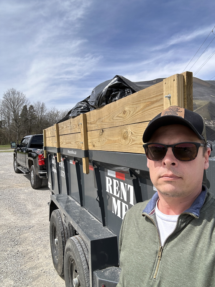 A man standing next to a loaded dump trailer with wooden extensions for junk removal by Salt Creek Disposal in Bowling Green, KY.