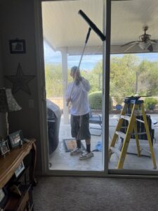 A handyman from Bring The Pane on a ladder, expertly cleaning a tall sliding glass door in Lewiston, ID.