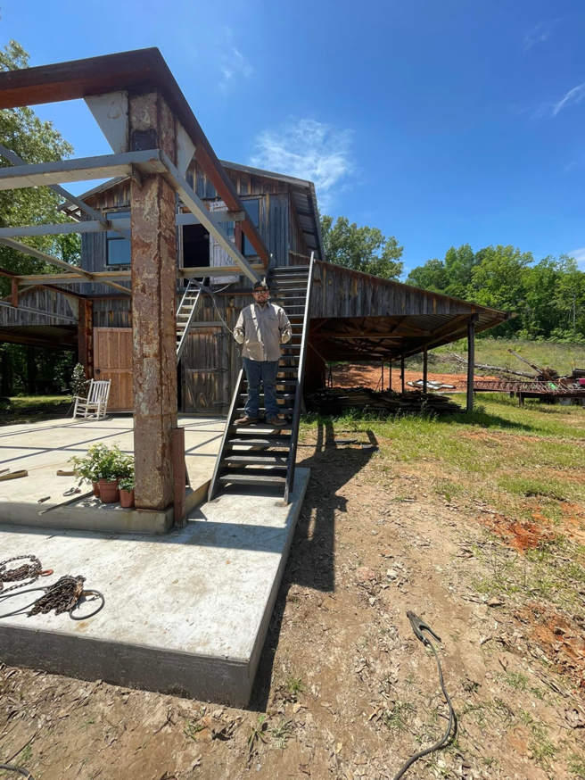 A man standing on newly installed metal stairs leading to a rustic building under construction by SJ Construction Services LLC in Austin, TX.