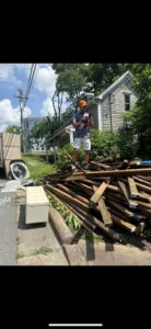 A Dumpzilla team member standing on a large pile of wood debris next to a truck for removal in Raleigh, NC.