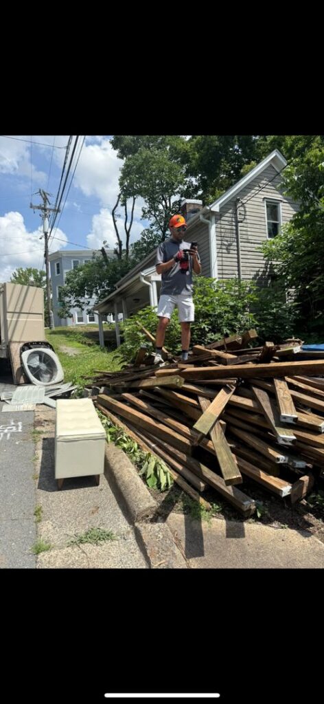 A Dumpzilla team member standing on a large pile of wood debris next to a truck for removal in Raleigh, NC.