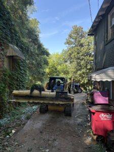 A man operating a compact track loader with a log grapple, moving a large log for Knotty Branches Tree Service in Macon, GA.