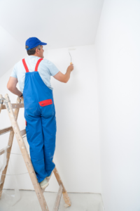 A handyman painting an interior wall from a ladder, provided by Coburns interior and exterior in Services Available In.