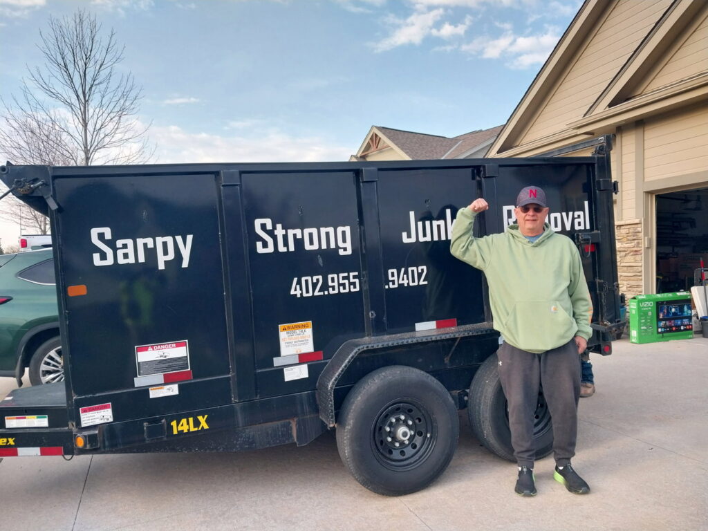 A man posing next to a Sarpy Strong Junk Removal dump trailer, representing Omaha Junk Removal services in Papillion, NE