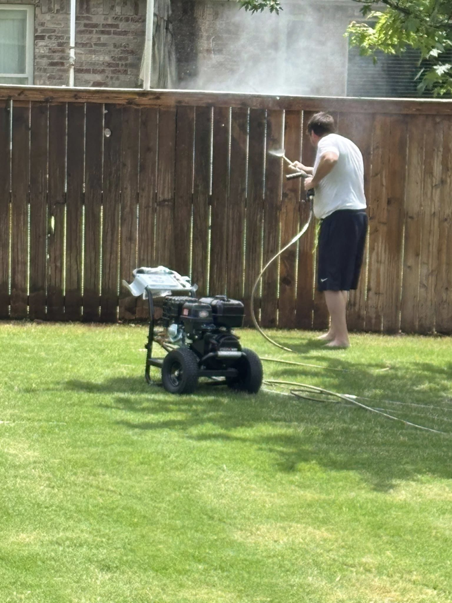 A handyman pressure washing a wooden fence with a professional machine for Precise Drain & Home Services in Springdale, AR.