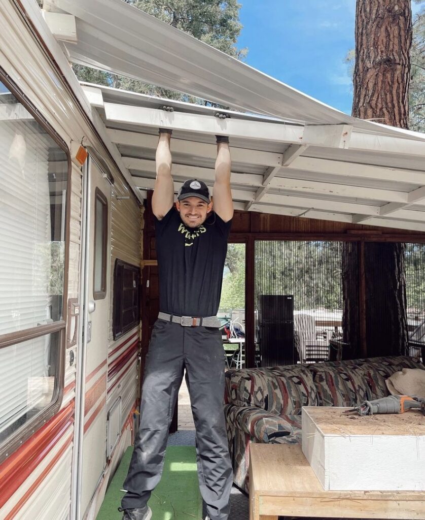 A man in a Junk Hunks 406 shirt actively removing a metal awning from an RV, demonstrating demolition or removal work in Missoula, MT.