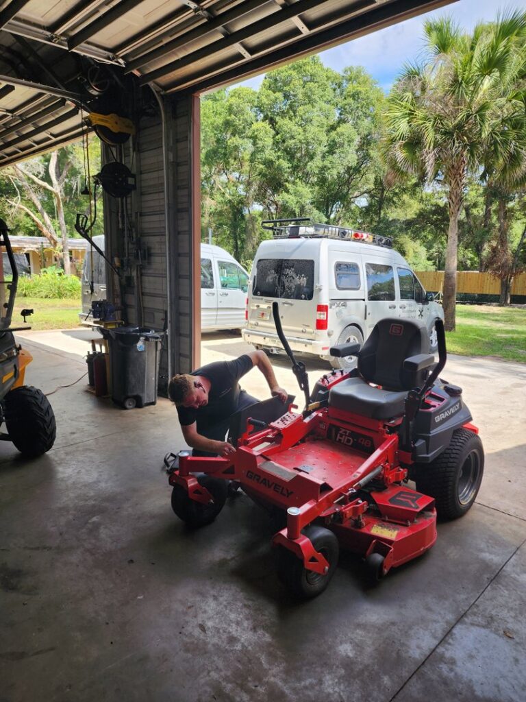 A man repairing a red zero-turn lawnmower inside a garage for Tim's Maintenance & Repair in Las Vegas, NV