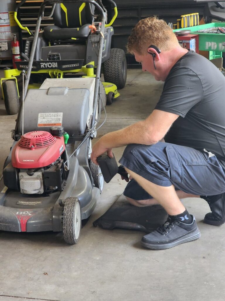 A man repairing a push lawnmower inside a garage for Tim's Maintenance & Repair in Las Vegas, NV