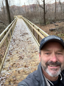 A man wearing a Wickcraft Boardwalks hat taking a selfie on a boardwalk during winter in Madison, WI.