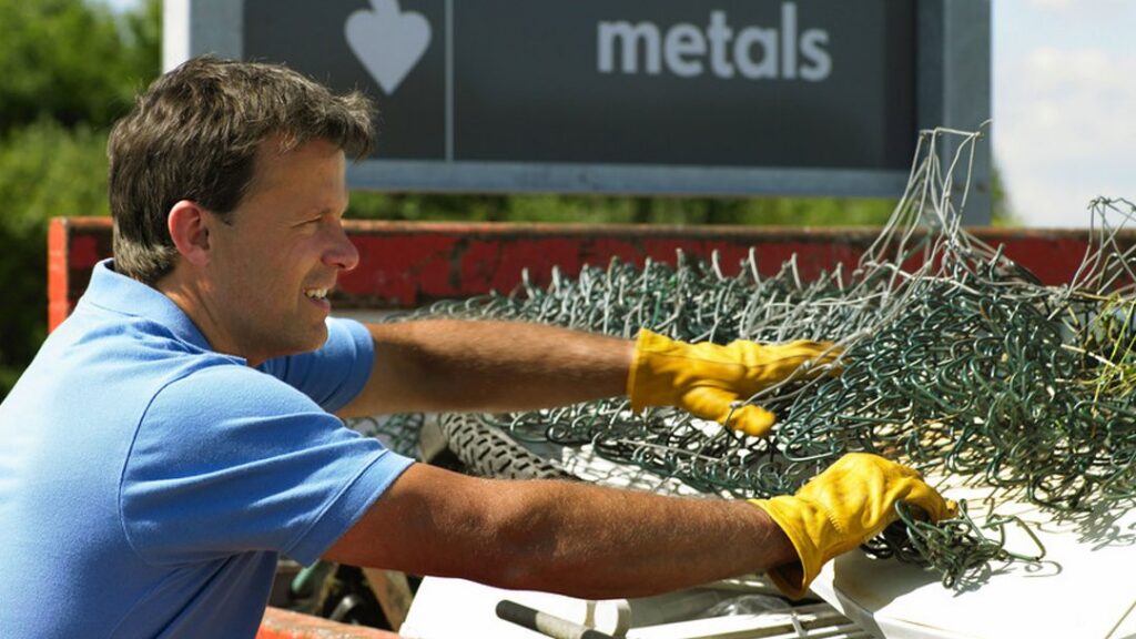 A man in work gloves sorting scrap metal into a container at Bailey Recycling and Scrap Metal in Topeka, KS