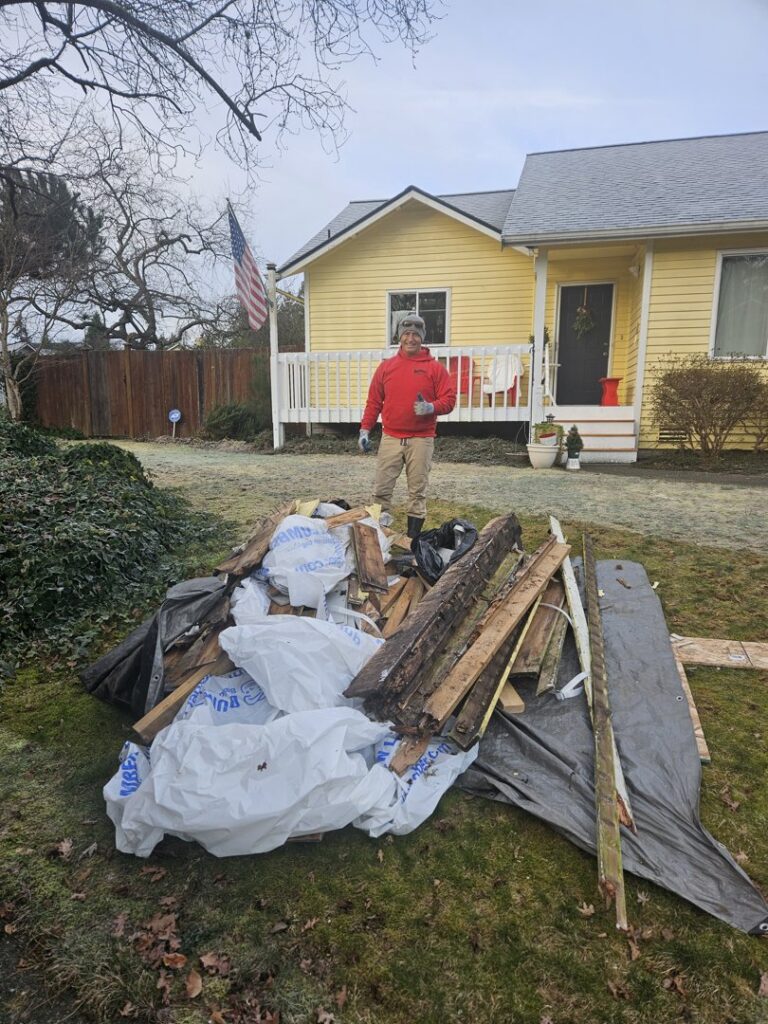 A Junkzilla Inc. team member standing next to a large pile of wood and construction debris in a residential yard in Everett, WA.