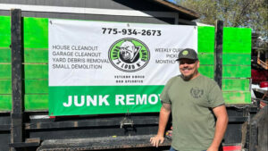A Grunts Load N Dump Junk Removal team member stands next to a truck with a service banner, ready for a job in Elko, NV.
