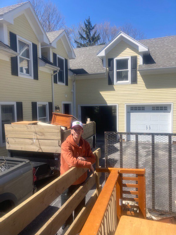 A man standing next to a trailer loaded with wooden furniture and items for removal by Hometown Hauling 802 in Milton, VT.
