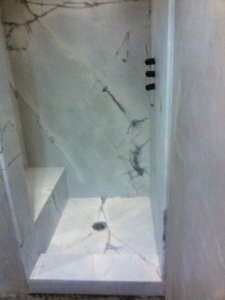 A newly installed shower stall with elegant marble-look walls, floor, and a built-in bench by Alfortish Marble & Granite, LLC in Baton Rouge, LA.