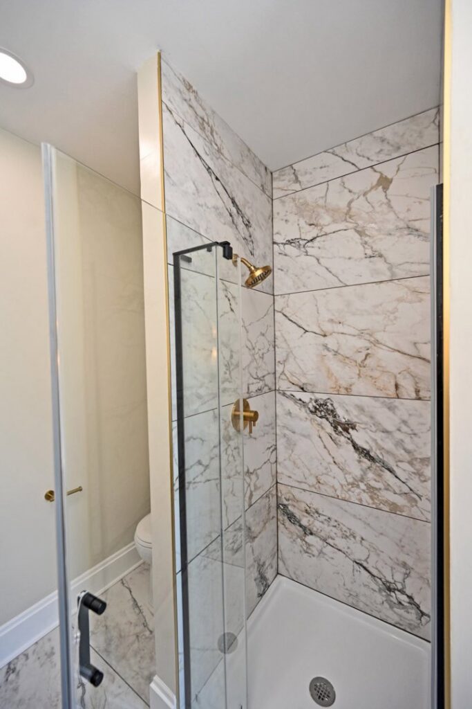 A newly installed shower with marble-look tiles and modern gold fixtures by Enjaycee Unlimited in Cincinnati, OH.