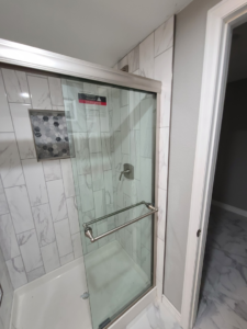 A close-up of a walk-in shower with white marble-look tiles and glass door by QCON LLC in Aurora, CO.