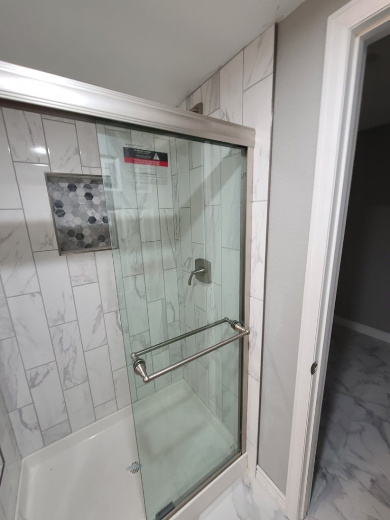 A close-up of a walk-in shower with white marble-look tiles and glass door by QCON LLC in Aurora, CO.