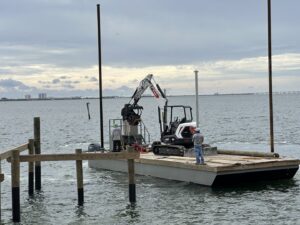 A barge with an excavator performing pile driving for marine construction in open water by Bayside Concrete & Construction in Tampa, FL