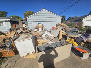 A massive pile of mixed junk, including furniture, construction debris, and appliances, in front of a garage for removal by Junk Away & Cleaning in Sacramento, CA.