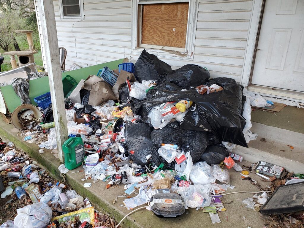 A massive pile of trash, bottles, and debris covering a porch, awaiting removal by Urban Junk Removal, LLC in Springdale, AR.