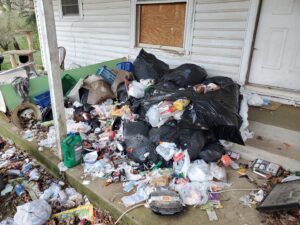 A massive pile of trash, bottles, and debris covering a porch, awaiting removal by Urban Junk Removal, LLC in Springdale, AR.