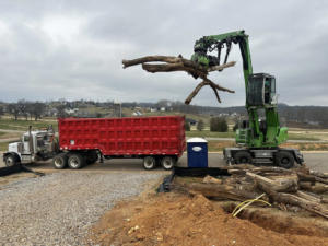 A material handler loads large tree trunks and branches into a dump trailer for 4M Tree Service in Knoxville, TN.