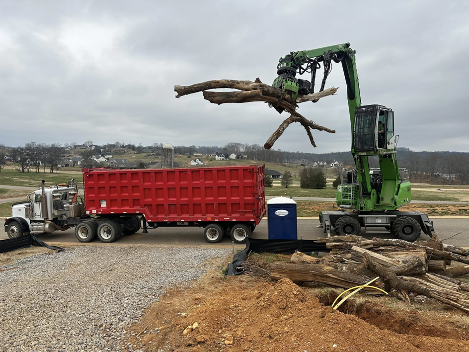 A material handler loads large tree trunks and branches into a dump trailer for 4M Tree Service in Knoxville, TN.