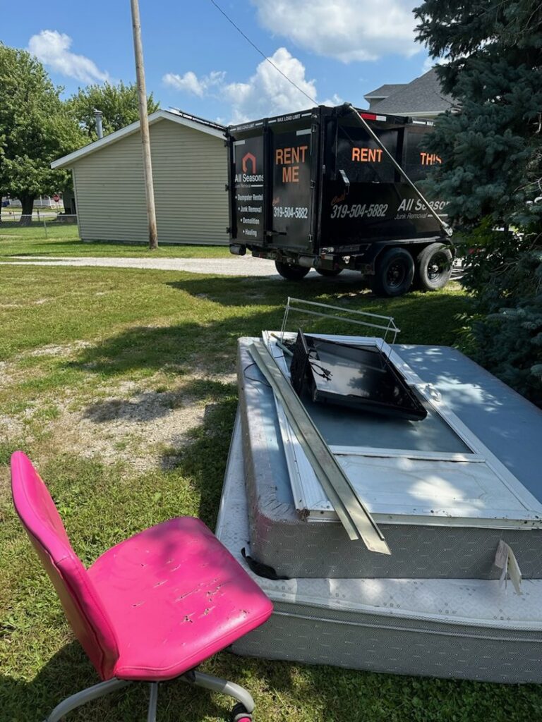 A mattress, pink chair, and other junk items piled on a lawn, ready for removal by All Seasons Junk Removal & Dumpster Services in Center Point, IA.