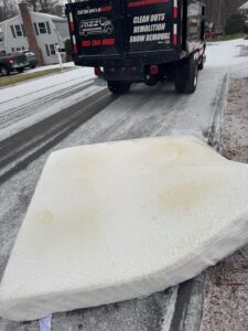 A mattress placed on the side of a snowy road with a Rizzo Junk Removal truck in the background, ready for pickup in Nashua, NH.