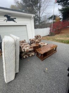Mattresses, a coffee table, and upholstered chairs placed outside a garage for junk removal by Rizzo Junk Removal in Nashua, NH.