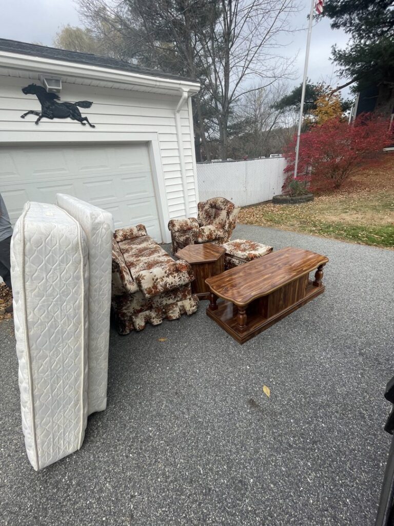 Mattresses, a coffee table, and upholstered chairs placed outside a garage for junk removal by Rizzo Junk Removal in Nashua, NH.