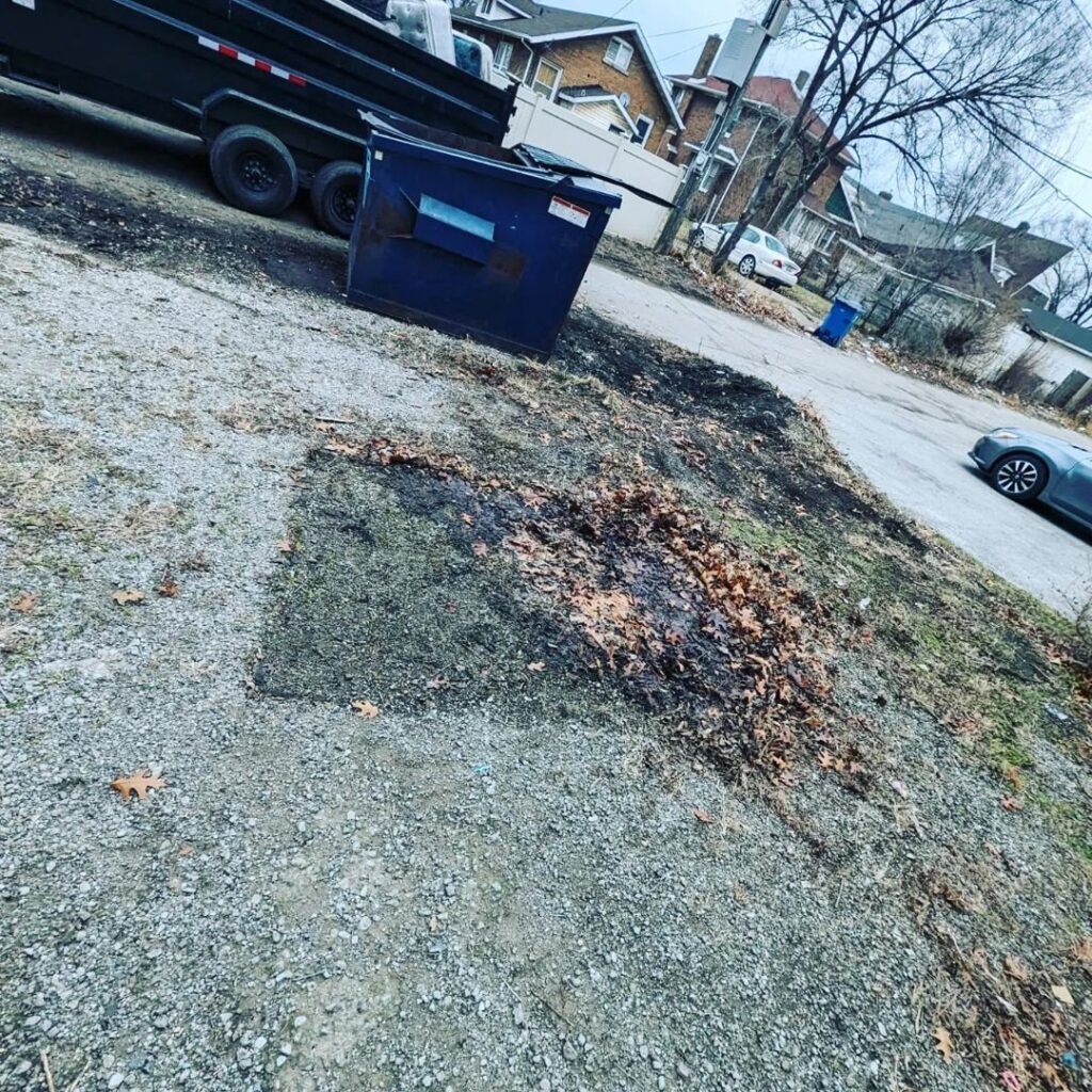 A large blue dumpster and a Merica JunkBoss LLC junk removal truck at a job site in Gary, IN.