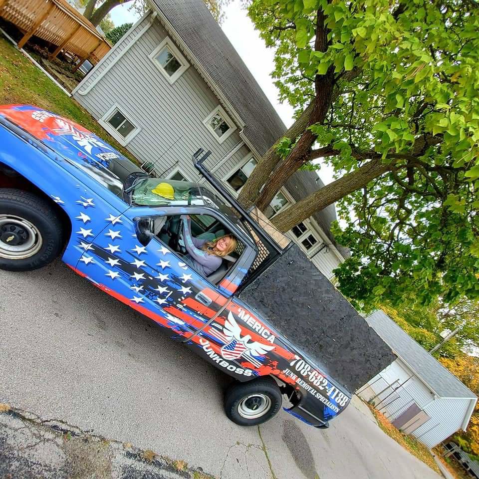 A smiling Merica JunkBoss LLC employee in the driver's seat of a branded junk removal truck in Gary, IN.