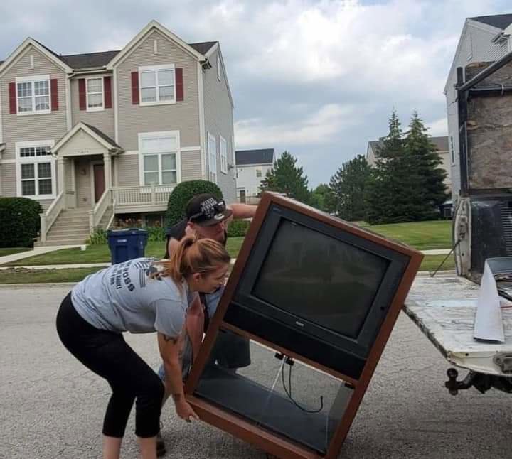 Two Merica JunkBoss LLC employees loading a large, old television into the back of a junk removal truck in Gary, IN.