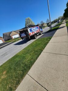 A Merica JunkBoss LLC junk removal truck driving on a residential street under a clear blue sky in Hammond, IN.