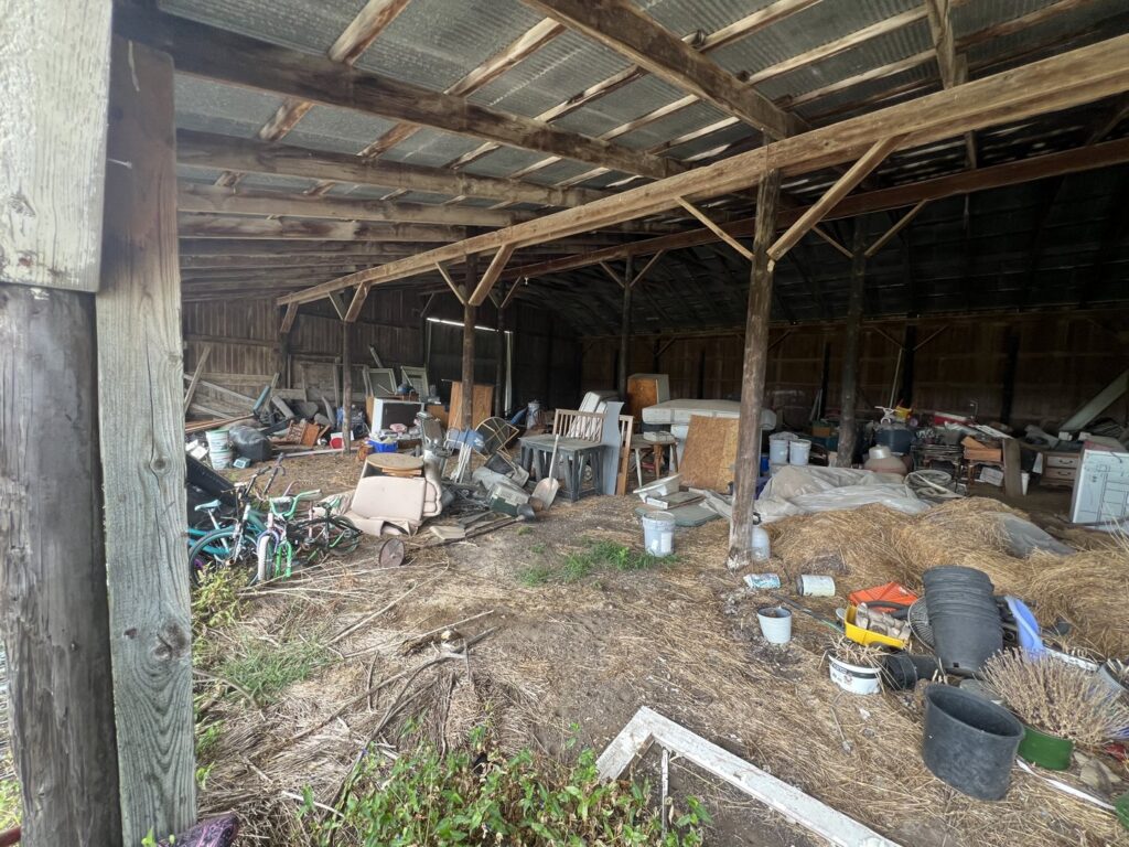 A messy barn interior filled with old furniture, debris, and various items, indicating a large junk removal job for Young Bucks Junk in Shawnee, KS.