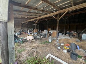 A messy barn interior filled with old furniture, debris, and various items, indicating a large junk removal job for Young Bucks Junk in Shawnee, KS.