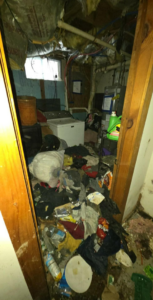 A messy basement filled with clothes and clutter, awaiting removal by CleanSite Solutions in Windham, ME.