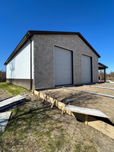 A metal building with a stone facade and roll-up doors under construction, with concrete forms in the foreground, by Southern Style Barns & Buildings LLC in Lake Charles, LA.