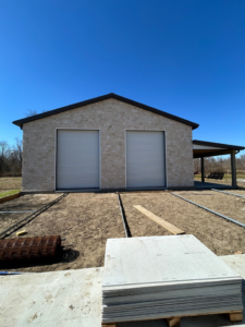 A metal building with a stone facade and two roll-up doors, with construction materials in the foreground, by Southern Style Barns & Buildings LLC in Lake Charles, LA.