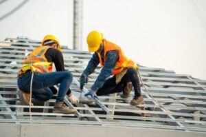 Two construction workers installing metal roof framing on a new building project by Total Improvements LLC in San Antonio, TX.