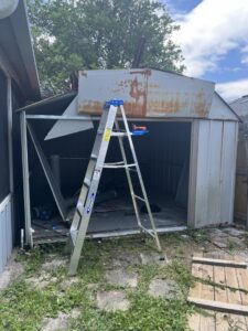 A metal shed partially dismantled with a ladder leaning against it, showing a demolition in progress by Junk Fade Away, LLC in Jacksonville, FL.