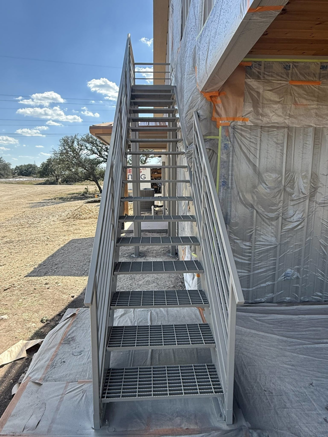 A newly installed metal staircase at a construction site, with the building exterior wrapped in protective sheeting, by Javier's Painting in San Angelo, TX.